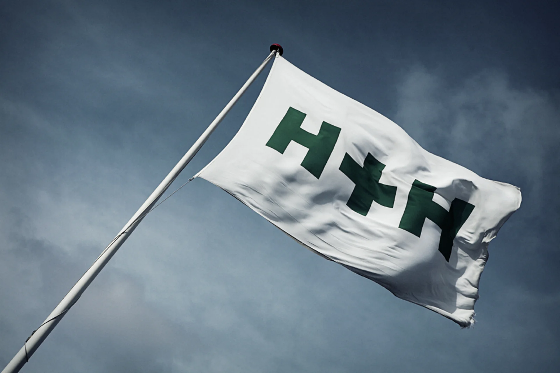 H+H company flag with logo viewed from a low-angle perspective against the sky
